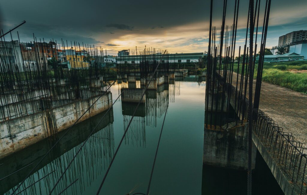 A serene view of an unfinished urban construction site reflecting on water at sunset.